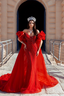 Woman in a red evening gown standing in front of a stone archway.