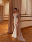 Woman in an elegant off-shoulder gown standing in a room with wooden flooring and decorative walls.